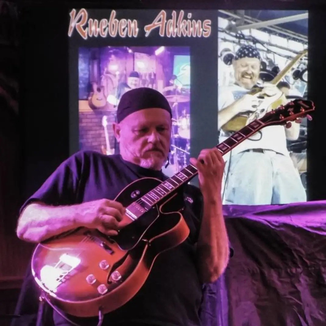 Reuben performing with electric guitar in front of his backdrop